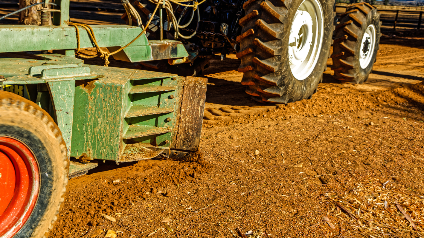 A tractor is parked in the dirt near a fence